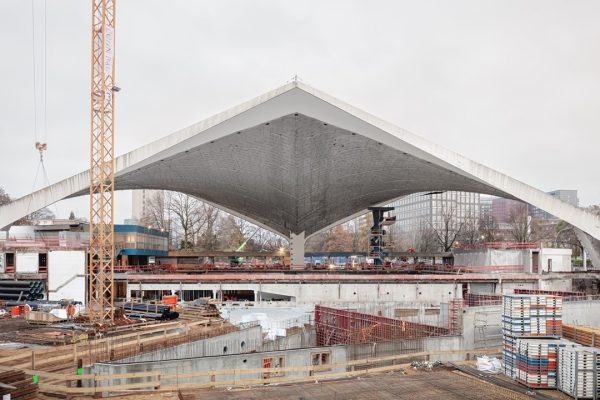 Geschwungenes Paraboloiddach aus Sichtbeton auf einer Großbaustelle mit einem hohen Baukran.