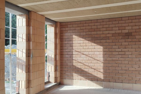Massive gemauerte Innenwand aus roten Ziegeln im Rohbau mit natürlichem Lichteinfall durch ein Fenster.