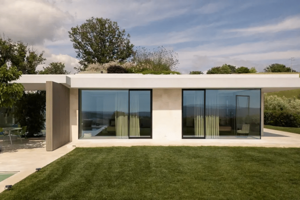 Moderne Villa F Glasfassade mit großen Fensterfronten, flachem Dach und gepflegtem grünem Rasen im Außenbereich.