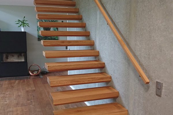Moderne Holztreppe EGO mit Wandhandlauf an einer Sichtbetonwand im minimalistischen Design.