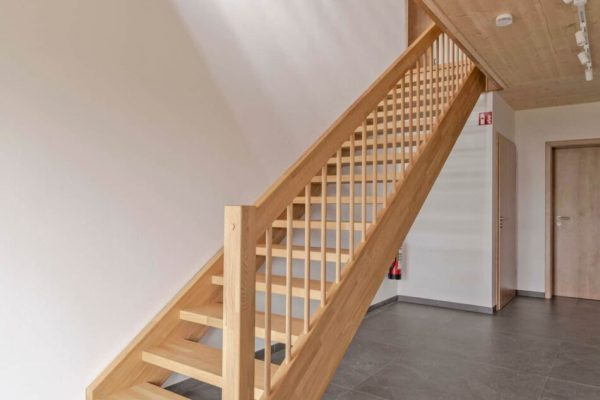 Moderne Holztreppe aus hellem Massivholz führt über graue Bodenfliesen in das lichtdurchflutete Obergeschoss.