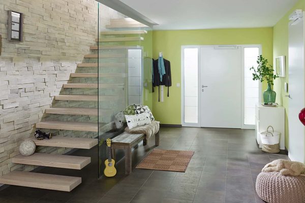 Moderne Kragarmtreppe EGO Zero mit Glasgeländer und Holzstufen vor einer hellen Natursteinwand.