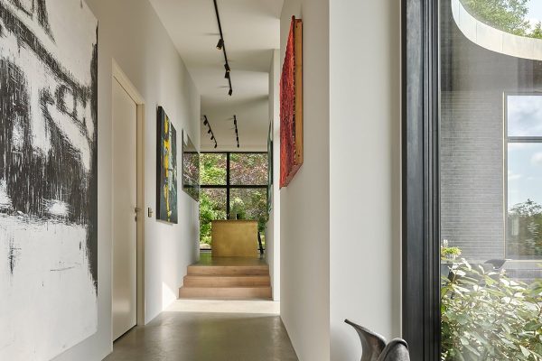 Moderner Flur im ADA House mit abstrakter Kunst, Holzstufen und Blick durch große Fenster in den Garten.