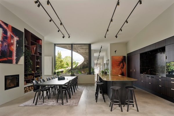 Modernes Interieur im ADA House mit dunkler Küche, Essplatz und markantem Panoramafenster mit Blick in den Garten.