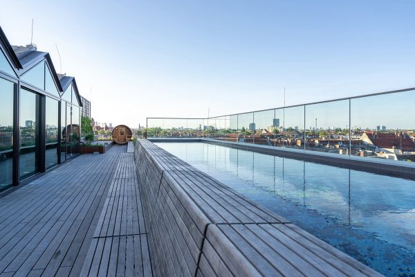Moderner Rooftop Pool auf der Dachterrasse mit Holzdeck und Glasgeländer über den Dächern der Stadt.