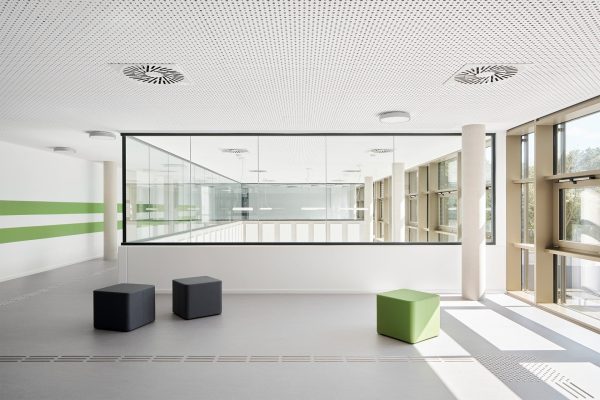 Moderne Innenansicht der Schule mit hellen Fluren, Glaswänden und bunten Sitzwürfeln für offenes Lernen.