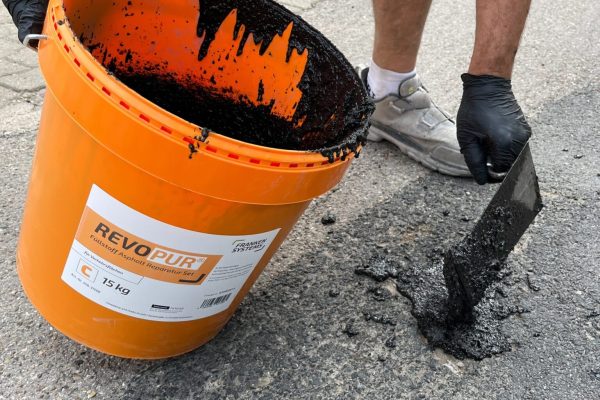 REVOPUR ARS Asphalt Reparatur Set wird mit einer Kelle gleichmäßig in einer Schadstelle auf dem Asphalt verteilt.
