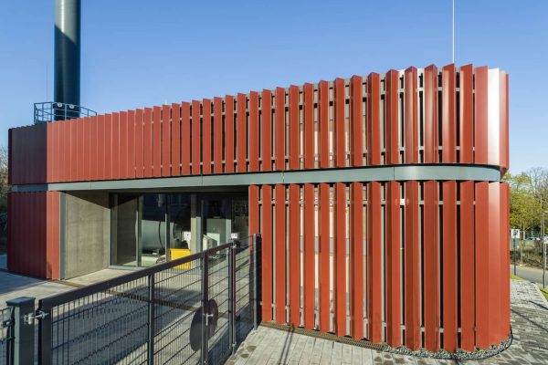 Entega Energiezentrale mit Metallfassade von BEMO aus roten vertikalen Aluminium-Lamellen vor blauem Himmel.