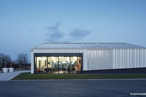 BEMO Stehfalzfassade aus Aluminium am Jöbstl Bürogebäude in RAL 9001 bei Dämmerung mit beleuchteter Glasfront.