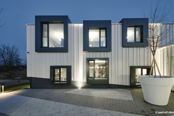 Moderne BEMO Stehfalzfassade aus Aluminium am Bürogebäude Jöbstl mit beleuchteten Fenstern bei Dämmerung.