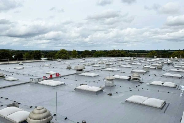 Flachdach der SBS Ecoclean Gruppe Monschau mit Lichtkuppeln und Lüftungsanlagen unter bewölktem Himmel.