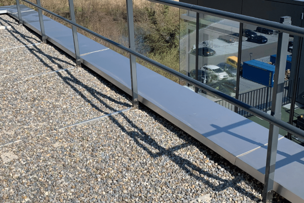 LUX-top G-T QUICK auflastgehaltener Kollektivschutz als Geländersystem auf einem bekiesten Flachdach.