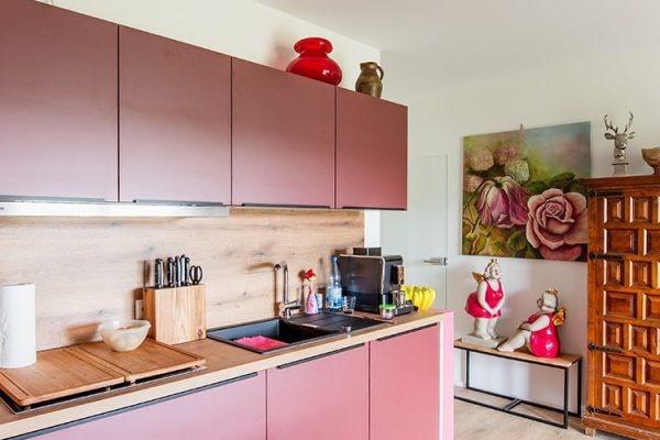 Weiße Infrarot-Deckenheizung in der Küche über einer modernen Küchenzeile mit rosa Fronten und Holzelementen.