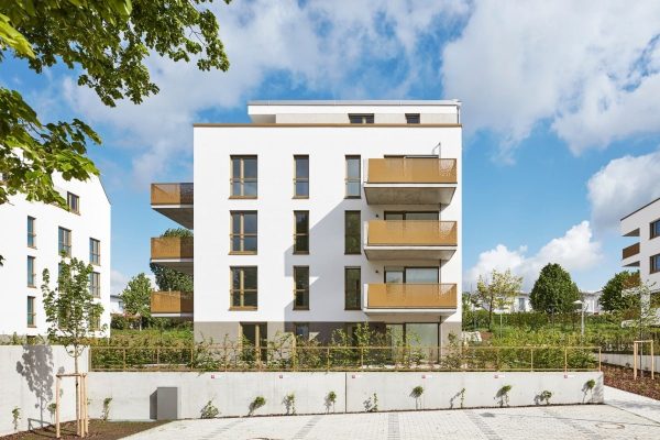 Moderne Wohnanlage Ludwigsburg mit weißer Fassade und markanten goldfarbenen Balkonen bei strahlendem Sonnenschein.