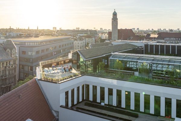 Moderne Dachterrasse in Berlin mit Sitzplätzen und Glaspavillon im Abendlicht über den Dächern der Stadt.