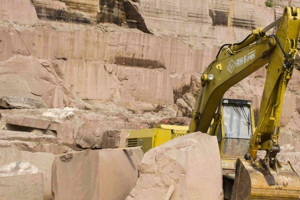 Gelber Bagger im Steinbruch Maulbronner Sandstein vor hohen Wänden aus rötlichem Naturstein.