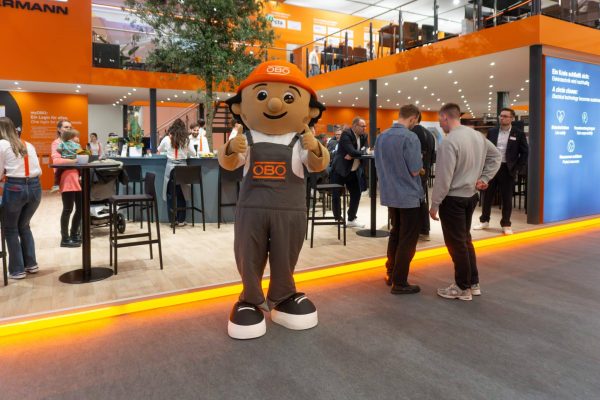OBO-Männchen mit Daumen hoch am Messestand der Light + Building 2026 für nachhaltige Elektrotechnik.