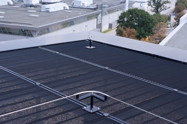 Pulverbeschichtete Anschlagpunkte auf einem Flachdach mit Gitterrost und integriertem Absturzsicherungssystem.