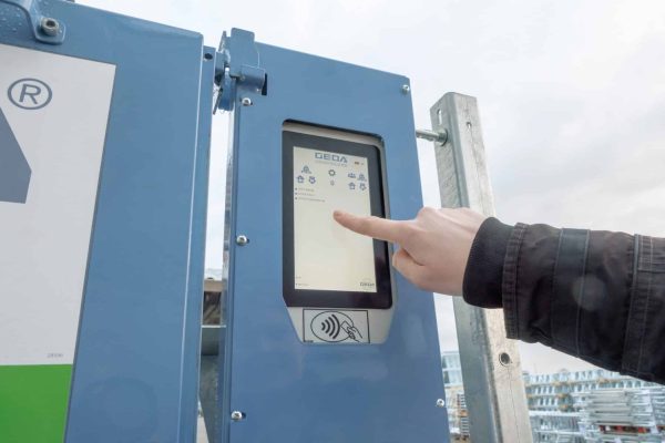 Eine Hand bedient das Display der GEDA IoT-Box PREMIUM an einer digitalen Steuereinheit im Außenbereich.