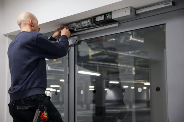 GEZE Service Techniker bei der Wartung der Antriebseinheit einer automatischen Glasschiebetür im Sportpark Freiham München