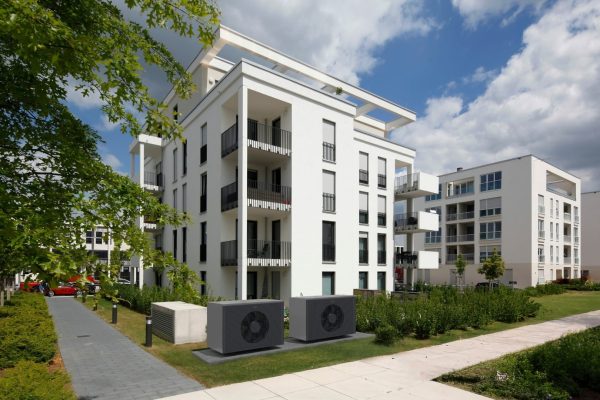 Zwei ELCO Wärmepumpen im schlanken Design vor einem modernen Mehrfamilienhaus zur effizienten Beheizung.