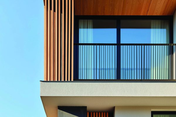 Geprüfte Balkongeländer Zebral an einer modernen Hausfassade mit vertikalen Holzlamellen vor blauem Himmel.