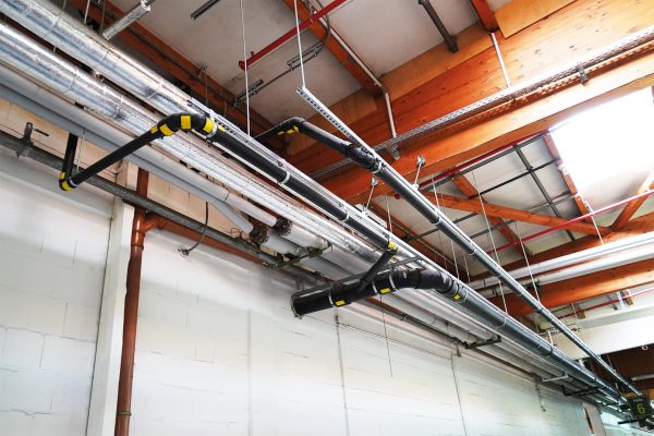 SitaPipe Druckströmungssystem an einer Industriehallendecke mit Holzträgern und weiteren Rohrleitungen.