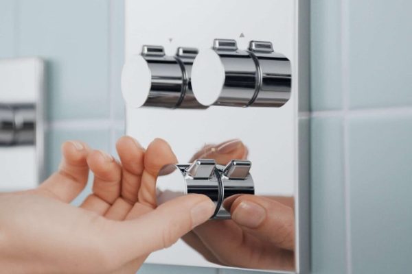 Eine Hand bedient die verchromte HANSA EASYMIX im Badezimmer vor einer hellblau gefliesten Wand.