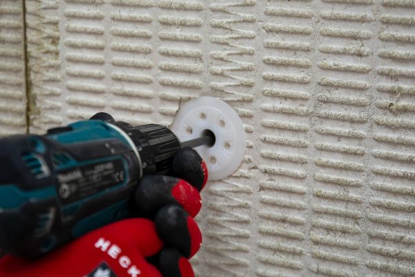 Handwerker beim Dämmplatten verdübeln an einer Fassade mit einem Akkuschrauber und weißen Kunststoffdübeln.