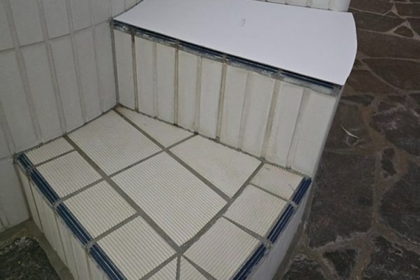 Weiße Whirlpool-Treppe mit blauen Akzenten auf dunklem Natursteinboden vor der Sanierung.