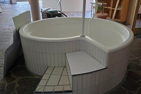Weißer gefliester Whirlpool mit Treppe und Handlauf im Spa-Bereich vor der Whirlpool Modernisierung.