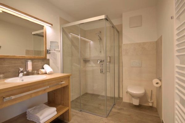 Modernes Badezimmer mit Glasdusche und Holzwaschtisch im Sport- und Wellnesshotel für Tradition und Moderne.