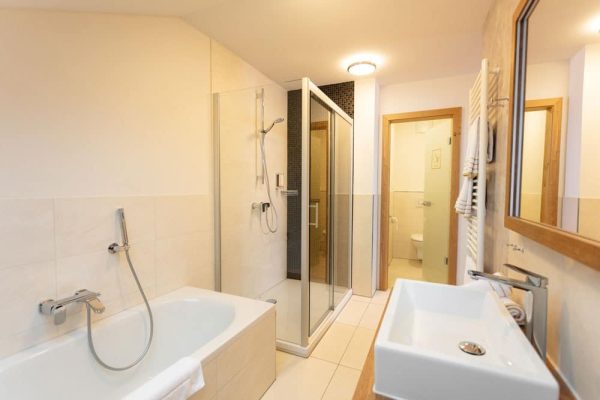 Modernes Bad mit Wanne und Glasdusche im Sport- und Wellnesshotel verbindet Tradition und Moderne.
