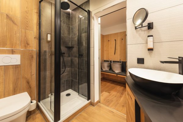 Modernes Bad im Sport- und Wellnesshotel mit Glasdusche, Holz und dunklen Fliesen vereint Tradition und Moderne.