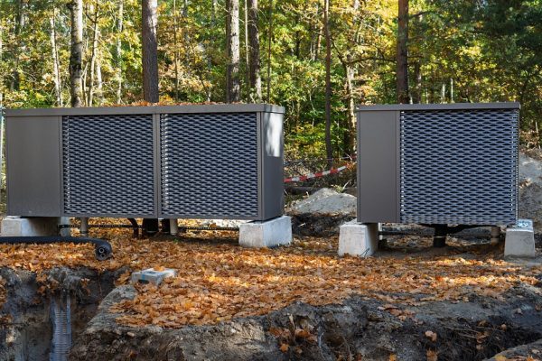 Moderne Erd-Wärmepumpen auf Betonsockeln im herbstlichen Wald während der Installation mit Erdarbeiten.