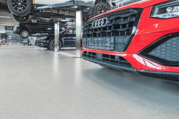 Homogener, ableitfähiger Boden in einer Industrie-Werkstatt mit Fahrzeugen auf Hebebühnen im täglichen Betrieb.
