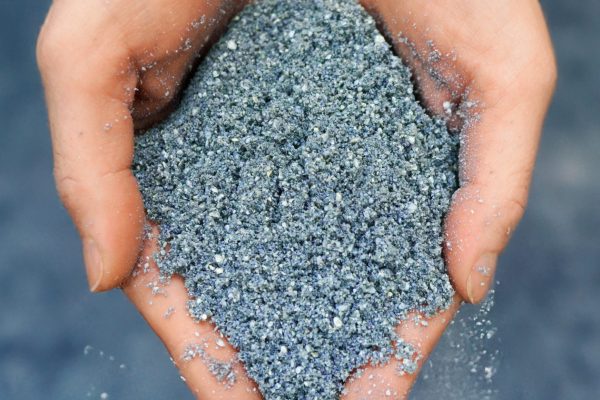 Hände halten das feinkörnige, blau-graue Insute 25-pro Granulat für professionelle Bauanwendungen.