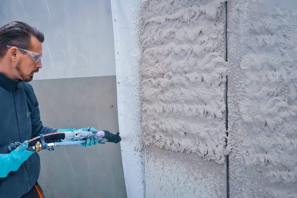 Handwerker mit Schutzbrille nutzt eine professionelle Putzmaschine zum Insute Dämmputz applizieren an einer Wand.
