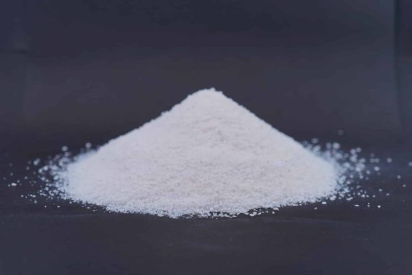 Weißes feinkörniges Granulat der Insute Flakes - Dämmputze aufgeschüttet auf einem dunklen Hintergrund.