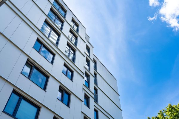 Moderne Fassade der James Hardie AC Panel Referenz München mit hellen Platten und Fenstern vor blauem Himmel.