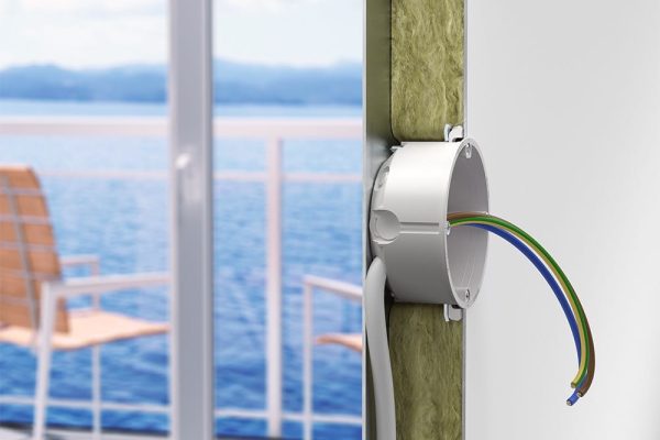 Hohlwanddose mit Kabeln zur sicheren Installation in Schiffbaupaneelen einer isolierten Wand vor dem Meer.