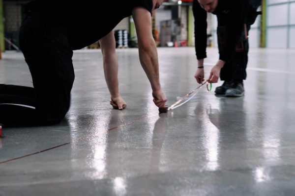 Zwei Handwerker installieren eine fachgerechte Erdungsanbindung mit Kupferband auf einem Industrieboden.