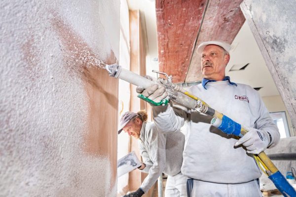 Handwerker bei der Knauf Rutesheim Putz Verarbeitung mit einer Putzmaschine auf einer Baustelle im Innenraum.