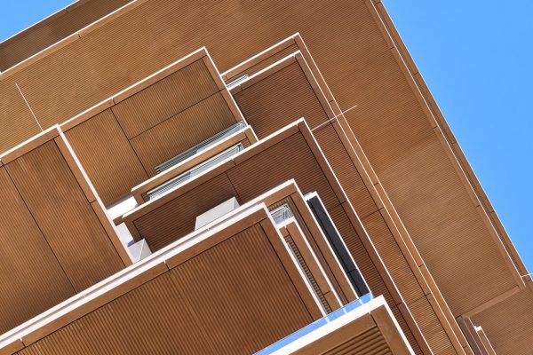 Moderne Fassade mit strukturierten Balkonuntersichten und braunen Balkonbrüstungen vor blauem Himmel.