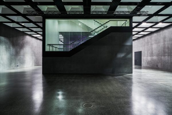 Fast unsichtbare OBO-Kassette im dunklen Boden eines modernen Ausstellungsraums mit Treppenaufgang.