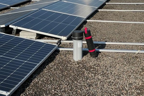 Installierter Sensor für dauerhaftes Monitoring für Dächer mit PV neben Solarmodulen auf einem flachen Kiesdach.