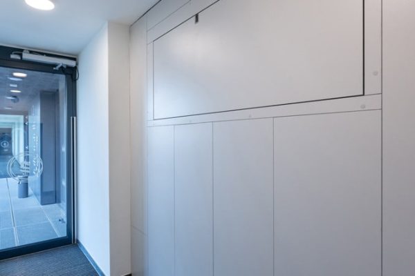 Flächenbündig integrierte horizontale Entrauchungsklappe in einer hellen Wandverkleidung im modernen Innenraum.