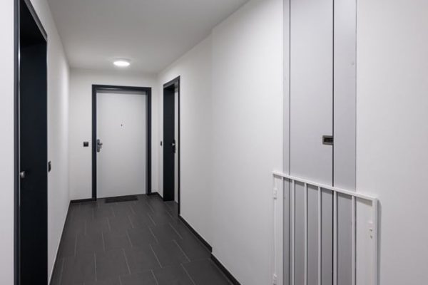 Schmale Entrauchungsklappen dezent in die Wand eines modernen Flurs mit dunklen Bodenfliesen integriert.
