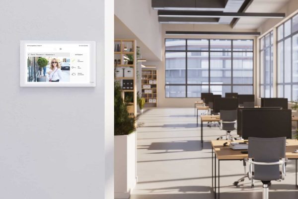 Gira Wohnungsstation Video IP für moderne Türkommunikation IP an weißer Wand in einem hellen Großraumbüro.