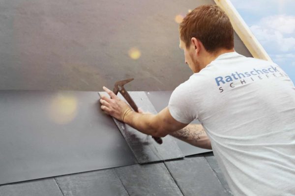 Dachdecker installiert die UltraRechteck-Deckung aus Schiefer fachgerecht mit einem Hammer auf einem Steildach.